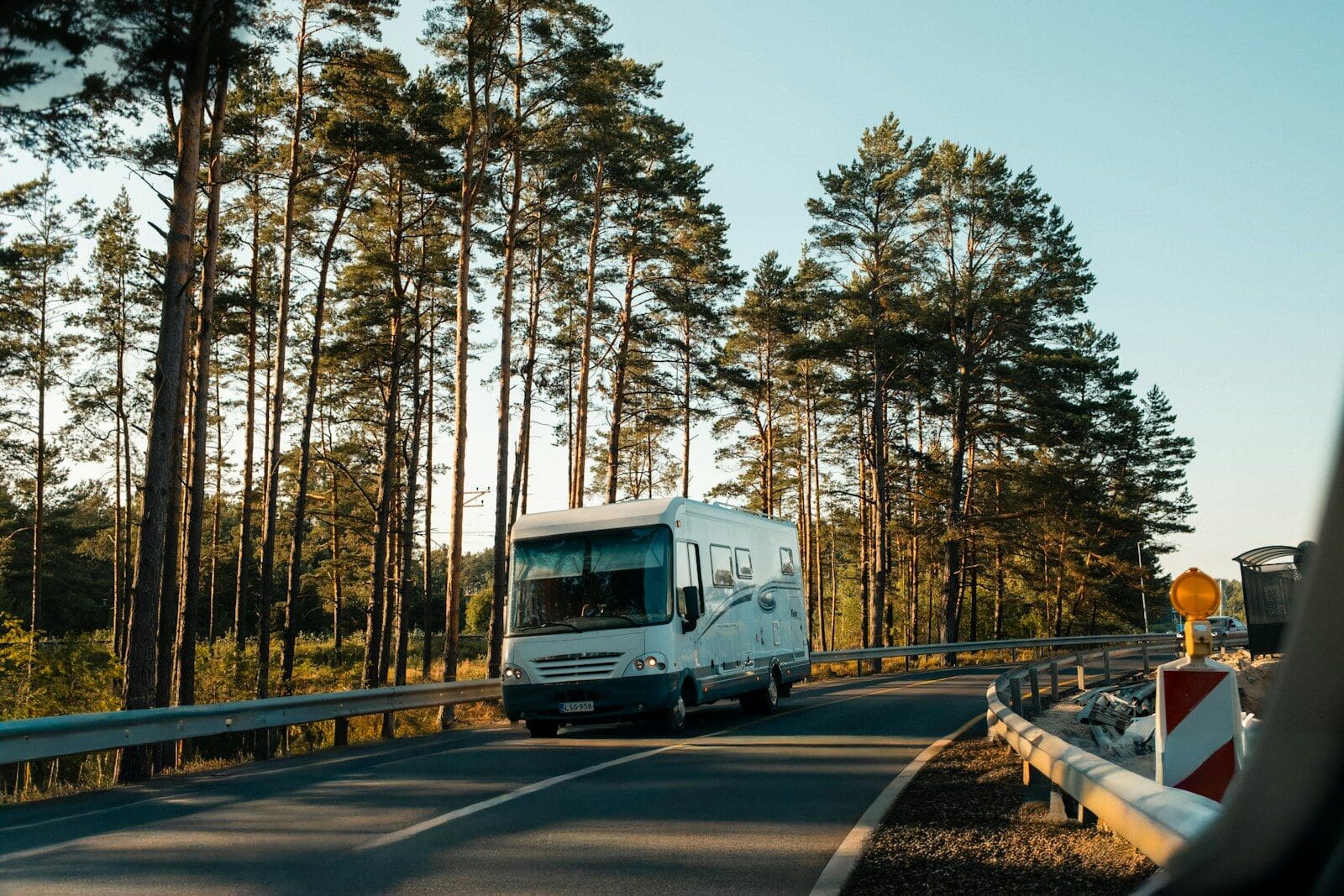 A white motorhome driving on a road lined with tall pine trees